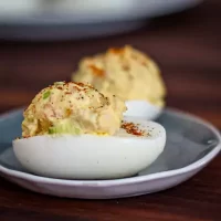Creamy deviled eggs with paprika topping on a dark plate.