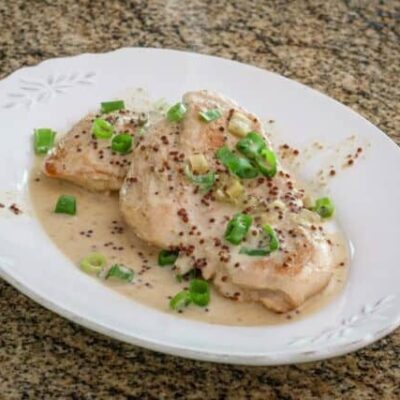 skillet dijon chicken with tarragon on a plate with green onion tops, garnishing it