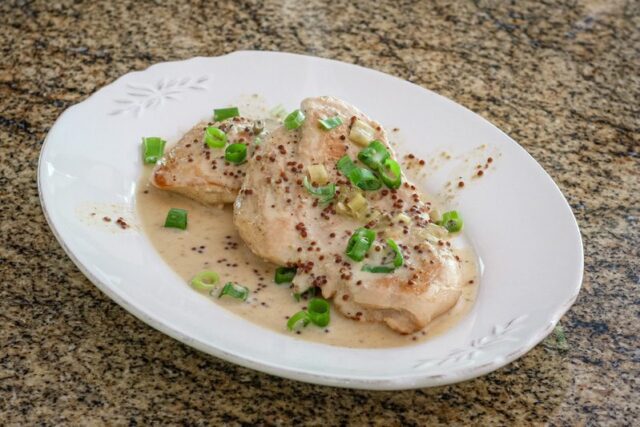 skillet dijon chicken with tarragon on a plate with green onion tops, garnishing it