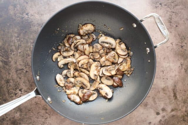 Sauteed sliced mushrooms in a black skillet.