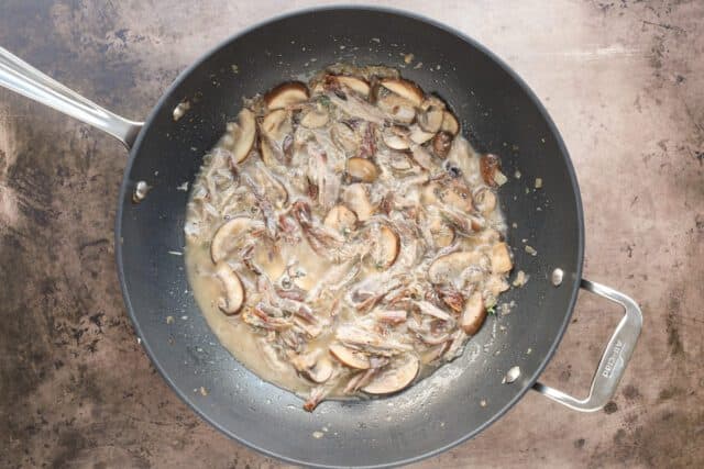 Adding the broth and shredded duck to the sauce for duck confit pasta.