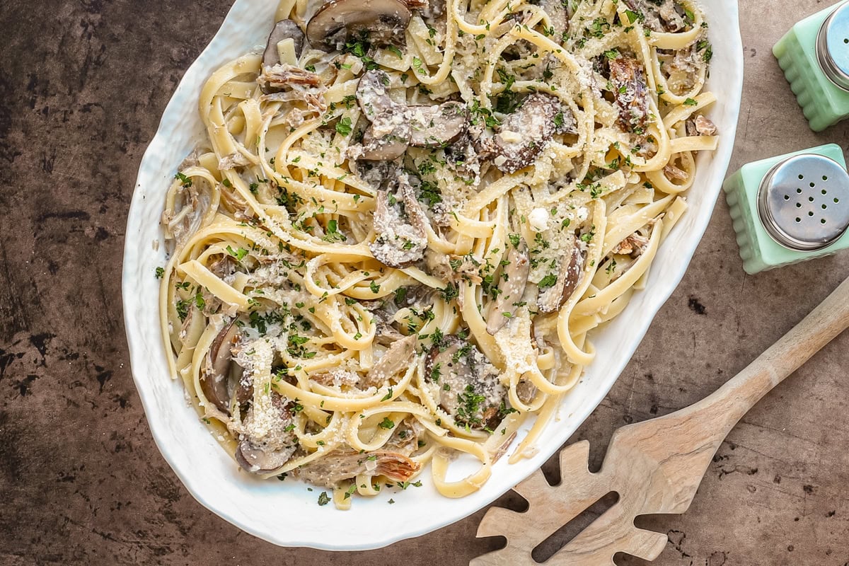 A serving dish of duck confit pasta made with duck confit legs, mushrooms garlic, shallots, fettuccine, garlic, cream, wine, and Parmesan cheese.