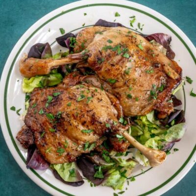 Roasted chicken drumsticks on a bed of mixed greens.