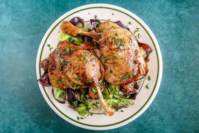 Roasted chicken legs on a bed of greens and herbs.