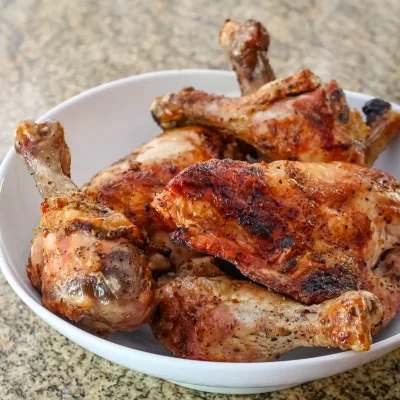 Juicy grilled chicken drumsticks in a white bowl on a granite countertop.