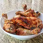 Cooked roasted chicken with crispy, seasoned skin and tender meat in a white bowl.