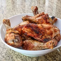 Cooked roasted chicken with crispy, seasoned skin and tender meat in a white bowl.