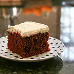 Rich red velvet cake with cream cheese frosting on a decorated plate.