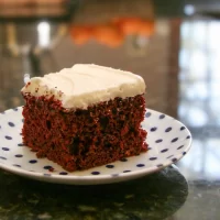 Rich red velvet cake with cream cheese frosting on a decorated plate.