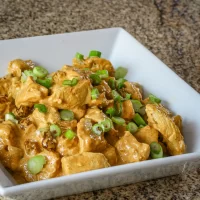 Crispy tofu with green onions in a white dish.