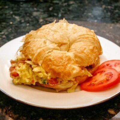 egg croissant sandwich with scrambled eggs, ham, and tomato