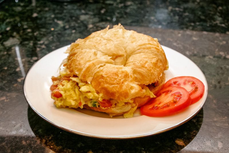 egg croissant sandwich with scrambled eggs, ham, and tomato