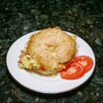 scrambled egg croissant sandwich on a plate with tomatoes