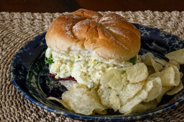 egg salad sandwich filling on a bun with lettuce and chips