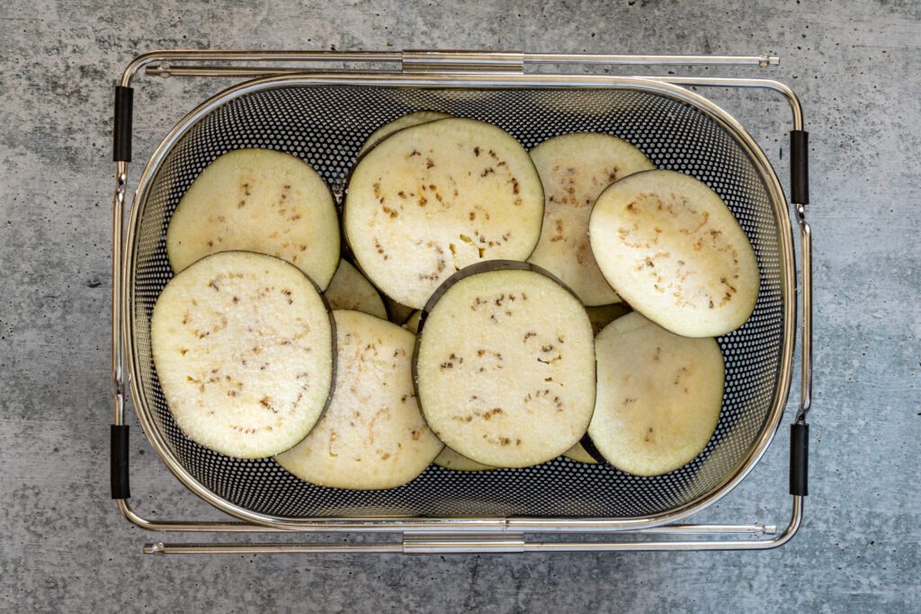 salted eggplant slices in a large colander