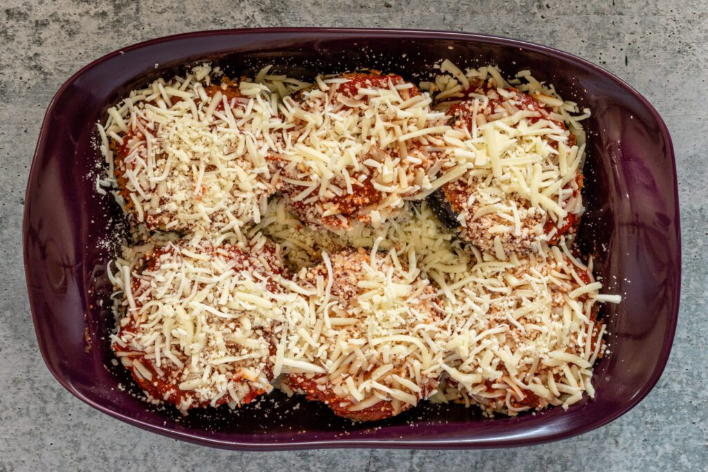 breaded and layered eggplant in the baking dish with cheese, ready to bake