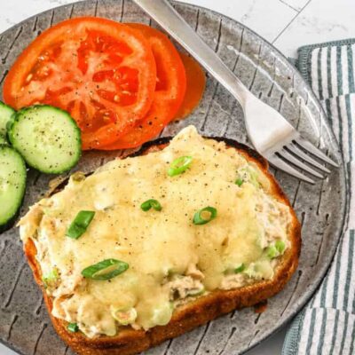 A tuna melt serving with sliced tomatoes and cucumbers on the side.