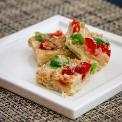 Cheesy vegetable pizza squares on a white plate.