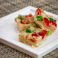 A plate of festive coconut shortbread squares with candied cherries and almonds.