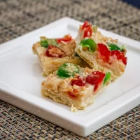 Crispy vegetable pizza bites with red and green peppers on a white square plate.