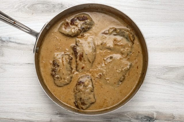 Succulent chicken thighs cooking in creamy mushroom sauce in a skillet.