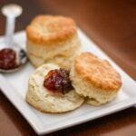 flaky buttermilk biscuits on a plate with one biscuit split with jam