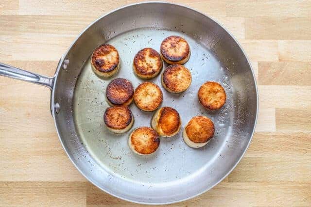 Golden fried scallops in a stainless steel skillet.