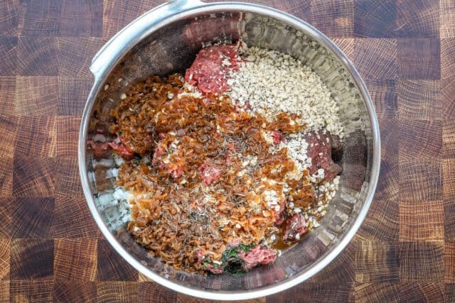 Mixed raw ground beef with seasonings in a metal bowl.
