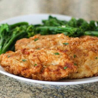 fried chicken breast cutlets on a plate with broccolini