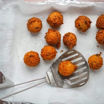 Golden fried croquettes on parchment paper with a slotted spatula.