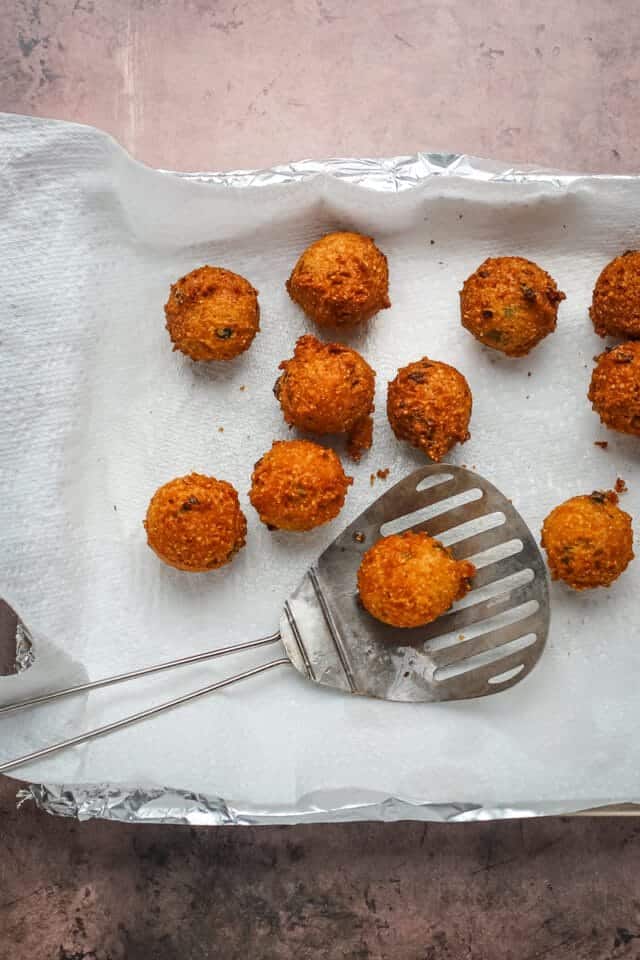 Golden fried croquettes on parchment paper with a slotted spatula.