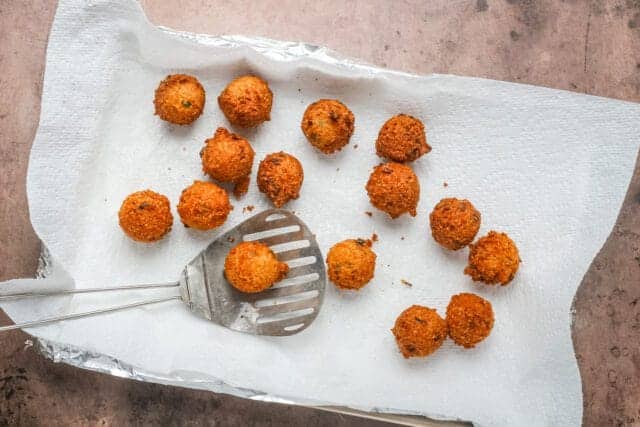 Golden crispy fried cheese balls on paper with slotted spoon.