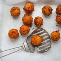 Golden fried appetizer balls on parchment paper with a slotted spatula beside them.