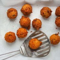 Crispy fried arancini balls on parchment paper with a slotted spatula.