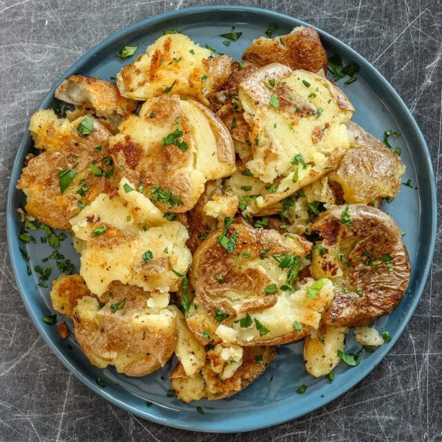 Fried smashed potatoes in a plate with garnish.