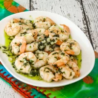 Bowl of cooked shrimp with garlic and herbs in olive oil.