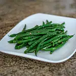 Steamed green beans seasoned with garlic on a white square plate.