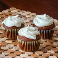 Frosted gingerbread cupcakes on a wooden mat.
