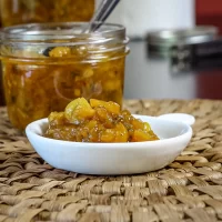 Sweet homemade apple chutney in a small white dish with a jar of chutney in the background.