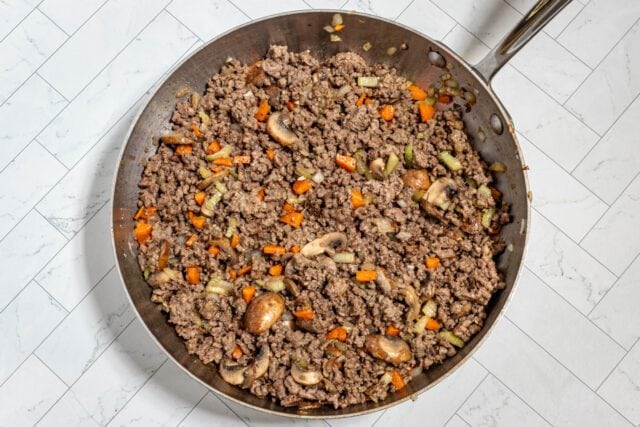 Ground beef with carrots and mushrooms cooking in a skillet.