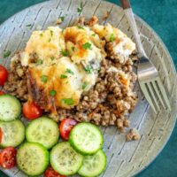 Baked mashed potatoes with herbs on a textured plate with fresh vegetables.