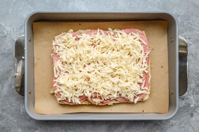 The ham and shredded cheese are added to the bottom half of the flat of rolls.