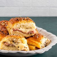 Savory biscuit sliders with melted cheese and ham on a white dish.