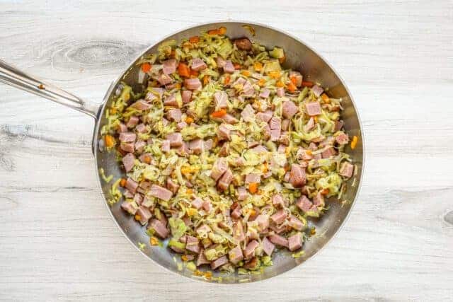 Sautéed ham, cabbage, and vegetables in a skillet.