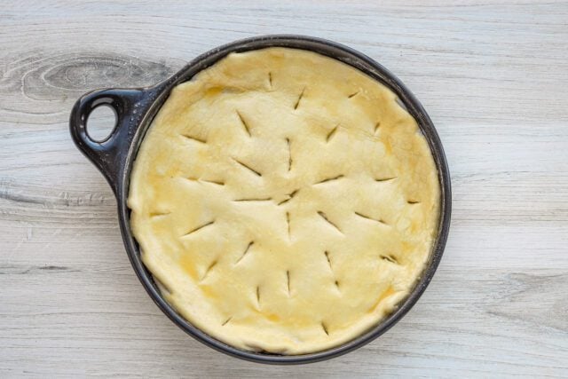Unbaked pie crust in a dark ceramic dish on a light wooden surface.