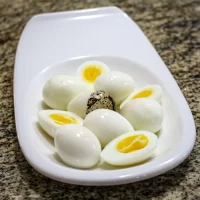 Boiled quail eggs served on a white dish with some cut in half.