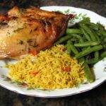 split chicken breasts roasted with lemon and herbs, on a plate with rice and green beans