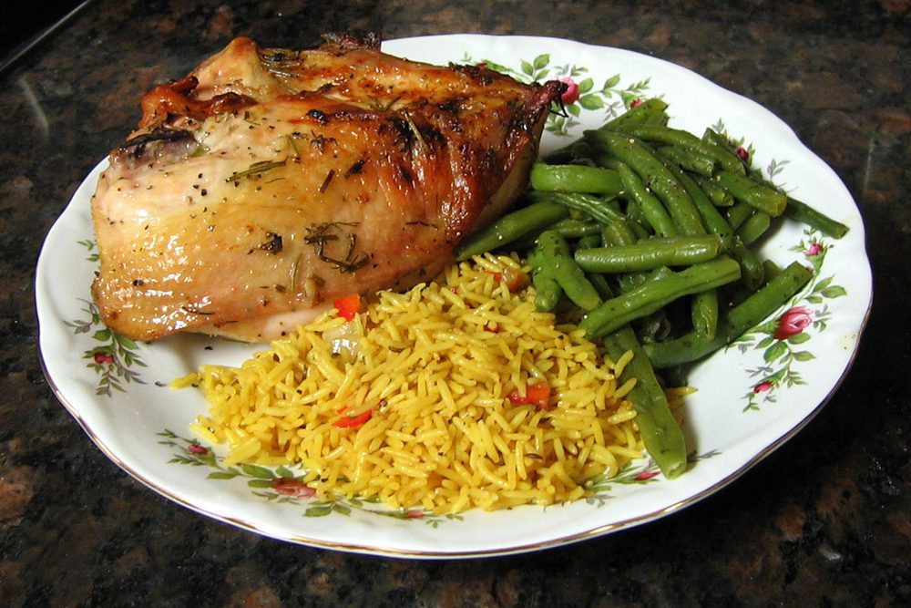 split chicken breasts roasted with lemon and herbs, on a plate with rice and green beans
