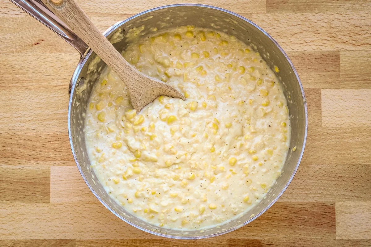 Creamy homemade cream-style corn in a saucepan with a spoon.