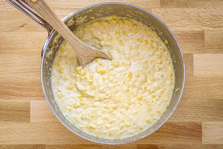 Creamy corn mixture in a metal bowl on a wooden surface.